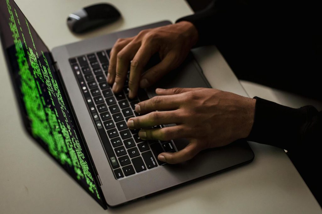 Crop cyber spy hacking system while typing on laptop.
